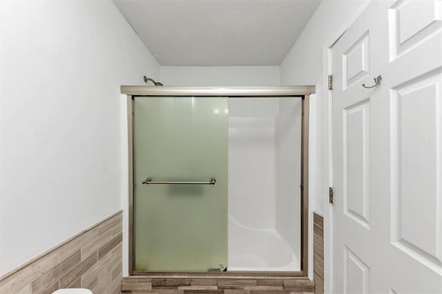 full bath with a shower with door, wood finished floors, and a textured ceiling