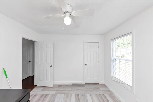 unfurnished bedroom with light wood-style floors, a textured ceiling, baseboards, and a ceiling fan