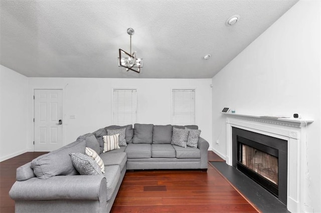 living room featuring wood finished floors, a fireplace with raised hearth, a textured ceiling, a chandelier, and baseboards