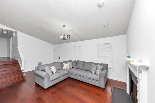 living area with dark wood-type flooring, baseboards, a fireplace with flush hearth, a chandelier, and stairs