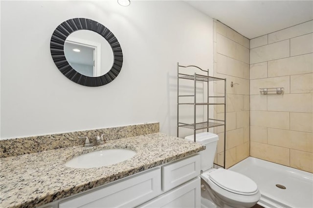 full bathroom featuring toilet, a tile shower, and vanity