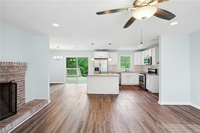 kitchen with appliances with stainless steel finishes, a brick fireplace, dark wood finished floors, baseboards, and recessed lighting