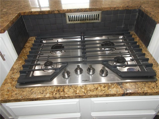 room details featuring stainless steel gas stovetop, tasteful backsplash, and white cabinetry