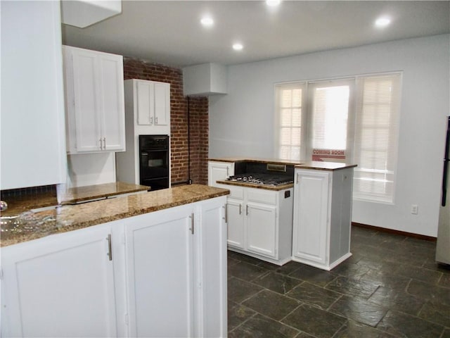 kitchen with white cabinets, light stone countertops, black double oven, and a center island