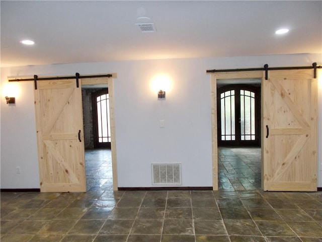 empty room featuring a barn door, a healthy amount of sunlight, and french doors