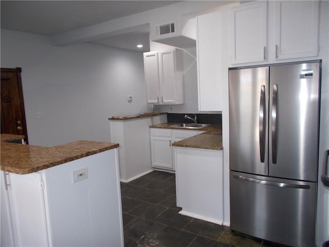 kitchen with sink, kitchen peninsula, white cabinetry, stainless steel refrigerator, and dark stone countertops