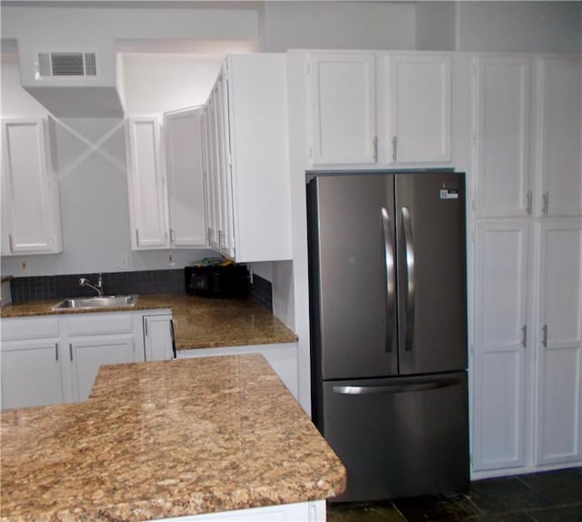 kitchen featuring white cabinets, light stone counters, sink, and stainless steel fridge