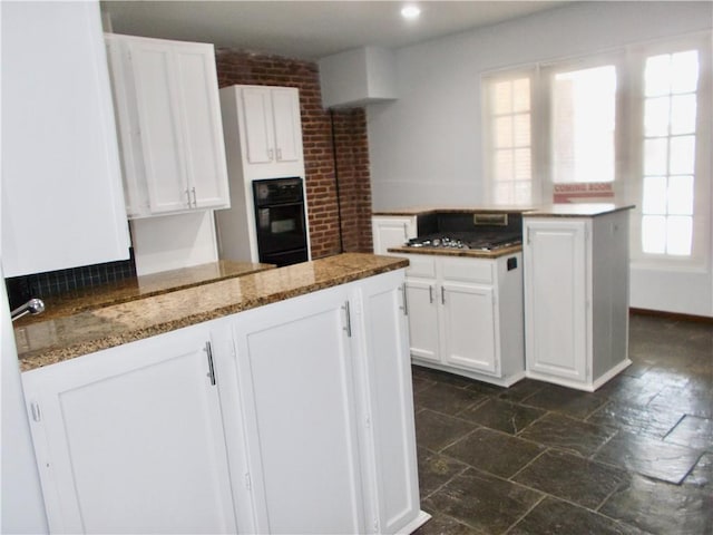 kitchen featuring brick wall, oven, stone counters, and white cabinets