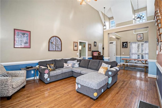 living room featuring wood-type flooring, ceiling fan with notable chandelier, and a high ceiling