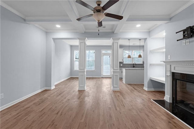 unfurnished living room with a wealth of natural light, decorative columns, light wood-style floors, and a fireplace with flush hearth