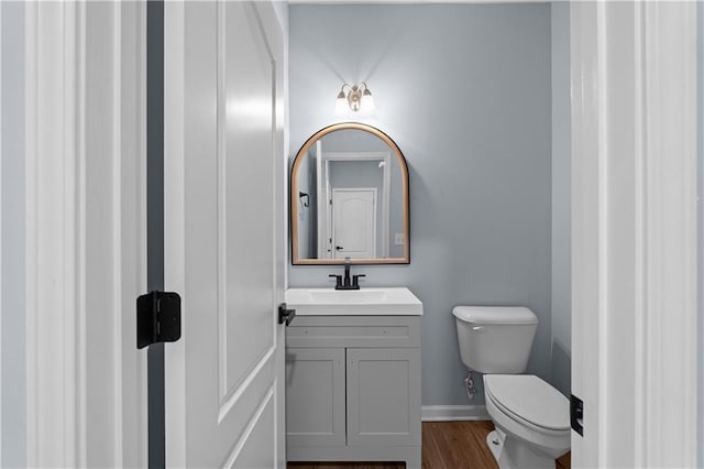 bathroom with toilet, vanity, baseboards, and wood finished floors