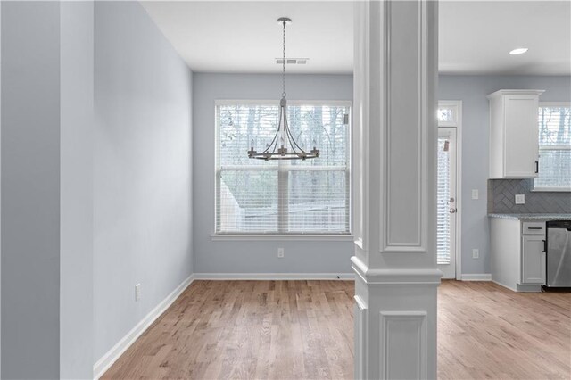 unfurnished dining area featuring visible vents, light wood-style flooring, an inviting chandelier, and baseboards