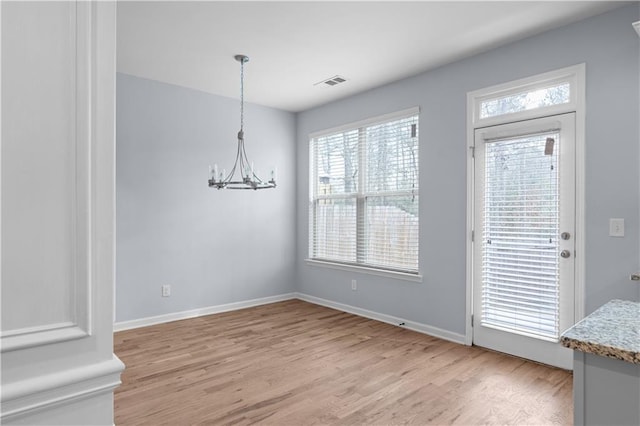 unfurnished dining area with visible vents, an inviting chandelier, baseboards, and light wood-style floors