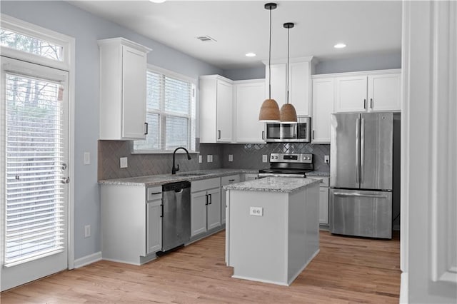 kitchen featuring a kitchen island, light wood-type flooring, appliances with stainless steel finishes, white cabinetry, and a sink