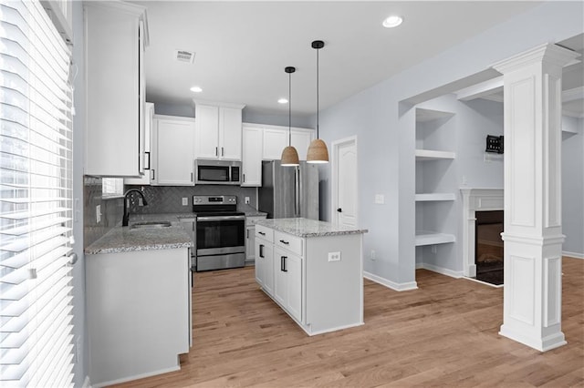 kitchen featuring a sink, a kitchen island, stainless steel appliances, light wood-style floors, and decorative columns