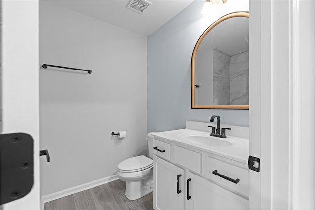 bathroom featuring visible vents, baseboards, toilet, wood finished floors, and vanity