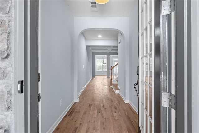 hall featuring beamed ceiling, stairway, arched walkways, light wood finished floors, and baseboards