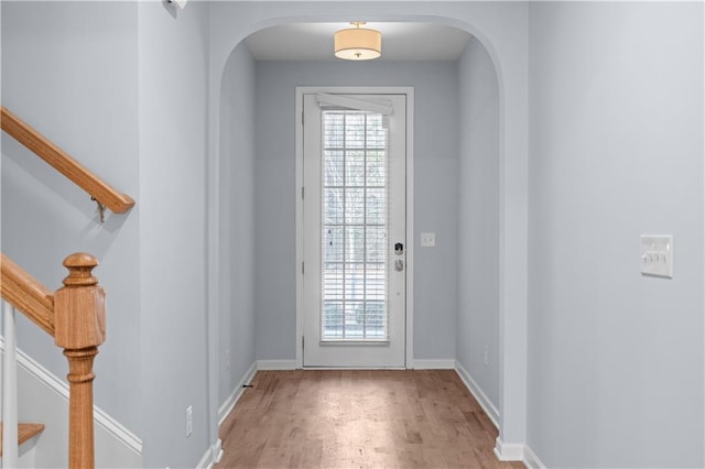 doorway featuring light wood-style floors, stairway, a healthy amount of sunlight, and arched walkways