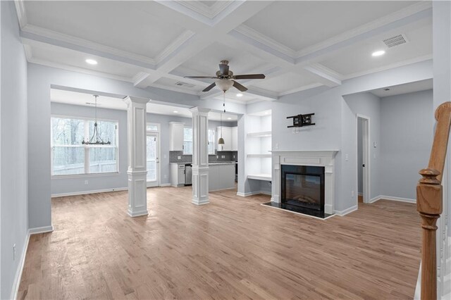 unfurnished living room with visible vents, ceiling fan with notable chandelier, a glass covered fireplace, light wood finished floors, and decorative columns