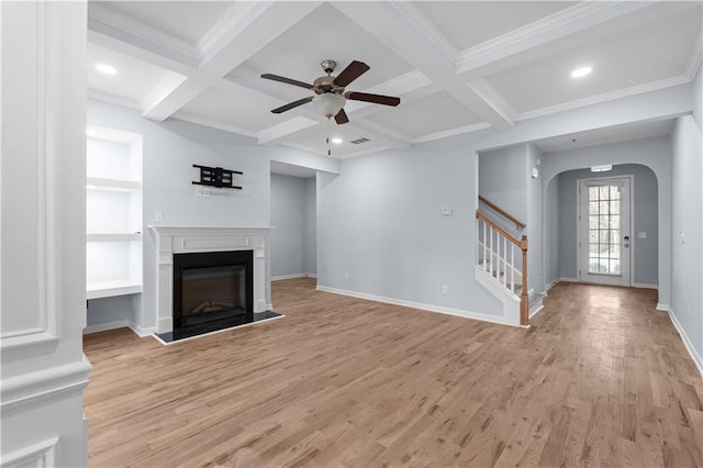 unfurnished living room with coffered ceiling, light wood finished floors, a fireplace with raised hearth, stairs, and beamed ceiling