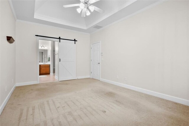 carpeted spare room featuring a barn door, a tray ceiling, ceiling fan, and ornamental molding