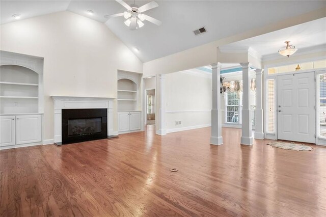 unfurnished living room with ornamental molding, built in shelves, ceiling fan with notable chandelier, high vaulted ceiling, and hardwood / wood-style floors