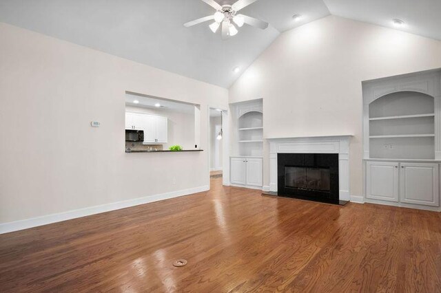 unfurnished living room featuring built in shelves, ceiling fan, wood-type flooring, and high vaulted ceiling