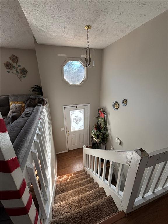 staircase featuring hardwood / wood-style flooring, a high ceiling, a textured ceiling, and an inviting chandelier