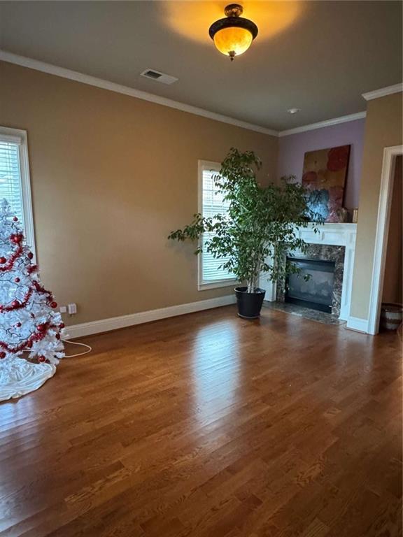 unfurnished living room with dark wood-type flooring, a healthy amount of sunlight, crown molding, and a high end fireplace