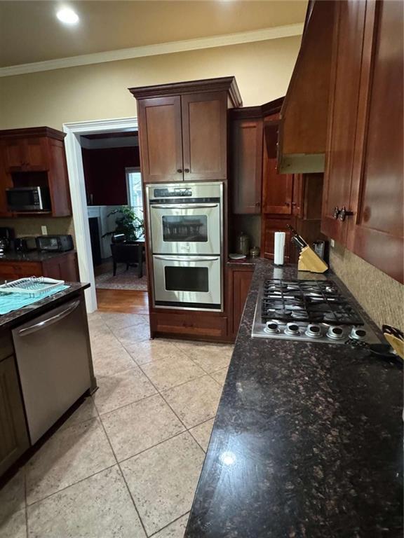 kitchen with dark stone countertops, light tile patterned floors, ornamental molding, and appliances with stainless steel finishes