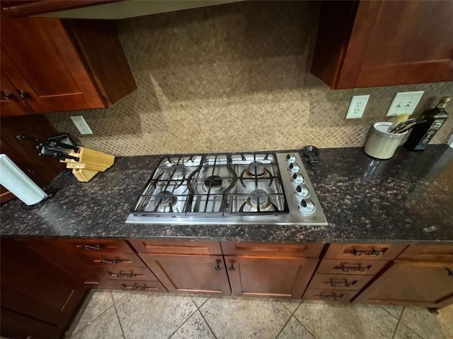 kitchen featuring tile patterned flooring, stainless steel gas cooktop, backsplash, and dark stone counters