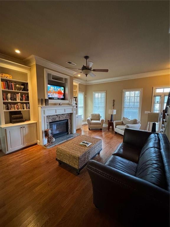 living room with ornamental molding, a stone fireplace, hardwood / wood-style floors, and a wealth of natural light