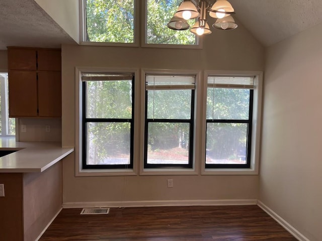 unfurnished dining area with dark wood-type flooring, an inviting chandelier, and vaulted ceiling