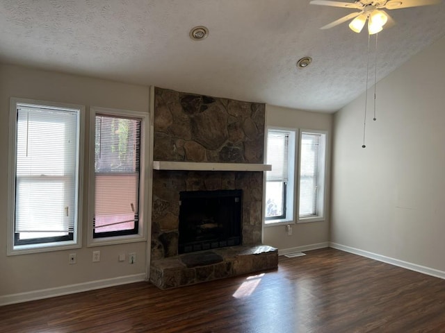 unfurnished living room featuring dark wood-type flooring, a stone fireplace, vaulted ceiling, a textured ceiling, and ceiling fan