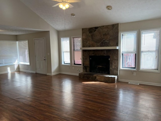 unfurnished living room featuring ceiling fan, dark hardwood / wood-style floors, a textured ceiling, a stone fireplace, and vaulted ceiling