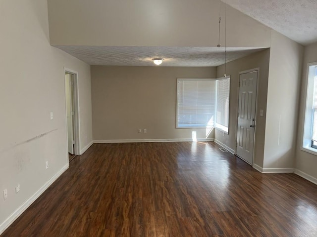 unfurnished room with dark hardwood / wood-style flooring, lofted ceiling, and a textured ceiling