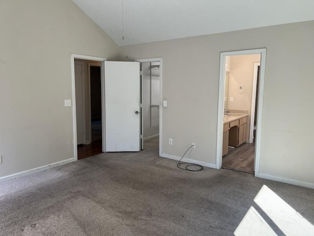 unfurnished bedroom with ensuite bathroom, a walk in closet, light carpet, and high vaulted ceiling