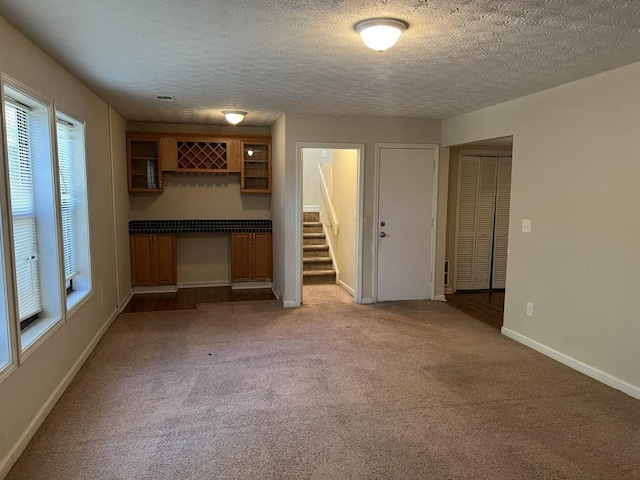 unfurnished living room with light carpet, bar area, and a textured ceiling