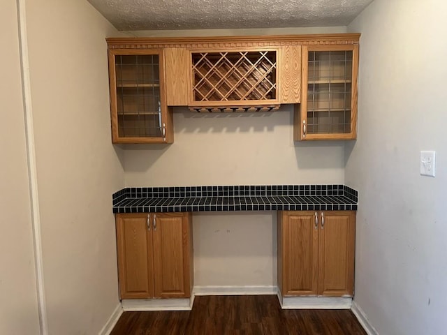 bar featuring tile counters, dark hardwood / wood-style flooring, and a textured ceiling