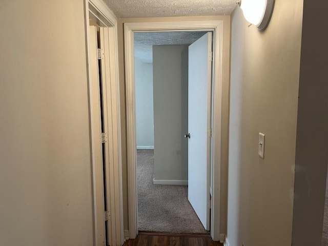 hall featuring a textured ceiling and dark colored carpet