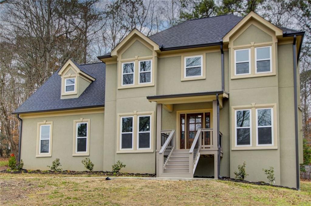 view of front of home with a shingled roof, a front lawn, and stucco siding