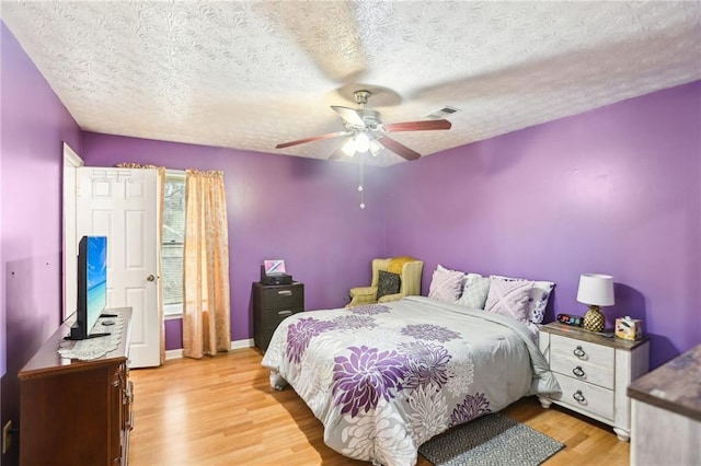 bedroom with a textured ceiling, light wood finished floors, a ceiling fan, and baseboards