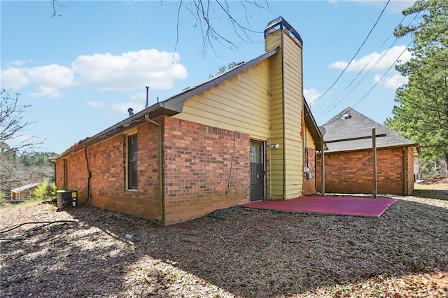 view of home's exterior featuring brick siding, a patio, a chimney, and central AC unit