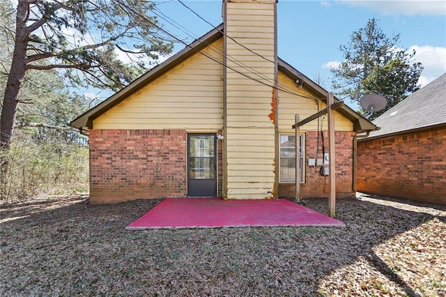 rear view of house featuring brick siding, a patio, and a chimney