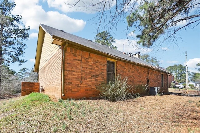 view of property exterior with central AC, brick siding, and a chimney