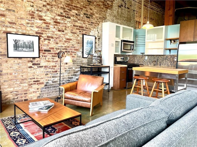 living area featuring finished concrete flooring, a high ceiling, and brick wall
