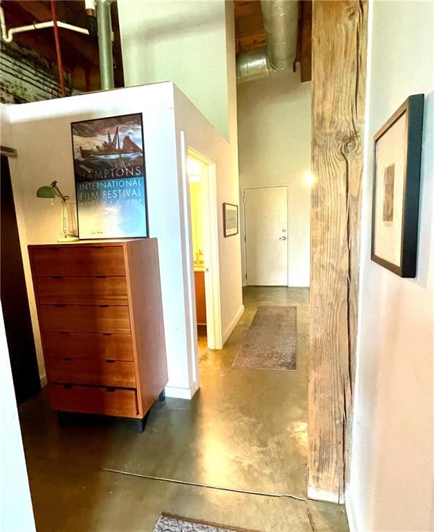 hallway featuring baseboards, concrete flooring, and a high ceiling