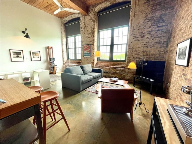 living room featuring a ceiling fan, brick wall, concrete flooring, wooden ceiling, and beamed ceiling
