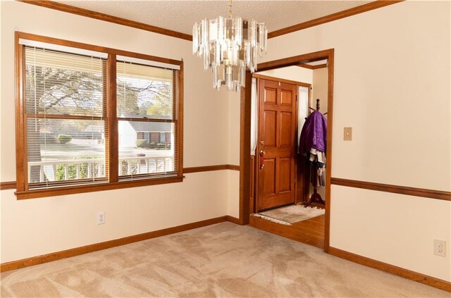 spare room with a textured ceiling, plenty of natural light, ornamental molding, a notable chandelier, and light colored carpet