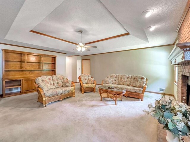 living room with a textured ceiling, ornamental molding, a brick fireplace, and a raised ceiling